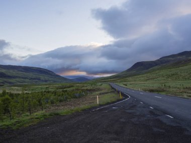 Asfalt yol eğrisi boş Kuzey yatay, yeşil çim renkli hills ve günbatımı dramatik gökyüzü, İzlanda Batı Highlands, kopya alanı dağlara yolu ile
