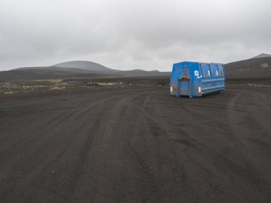 İzlanda, tepeler ve gri gökyüzü arka plan, kopya alanı siyah lav Kum Çölü'nde tek başına duran mavi metal çöp konteyner
