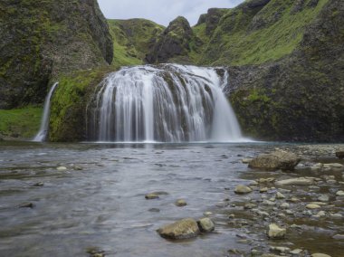 Güzel Stjornarfoss şelale kayalar, nehrin akışı yeşil kayalıklarla ve tepeler, yosun ve mavi gökyüzü, Kirkjubeajarklaustur kamp yakınındaki south Iceland'deki / daki uzun pozlama hareket bulanıklığı