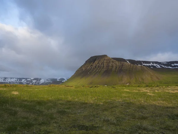 美しい雪覆われた崖山と Fljotavik コーブ ホットンストランディル 西フィヨルド アイスランド 緑の草の牧草地 黄金時間光 青い空を背景に丘の表示します — ストック写真
