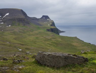 güzel kar yeşil uçurum ve mavi deniz ufuk büyük taş taş ve yeşil çim çayır, moody gökyüzü arka plan, Hornstrandir, Batı fjords İzlanda benekli