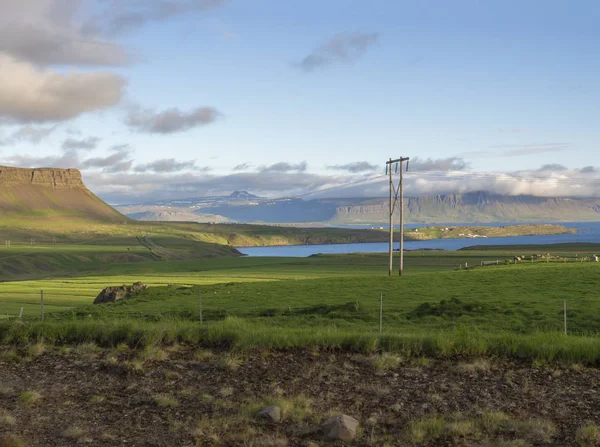 Paisaje rural del norte con hierba verde y colinas volcánicas, poste alino, nubes azules del cielo, hora dorada, verano en Islandia fiordos del oeste —  Fotos de Stock