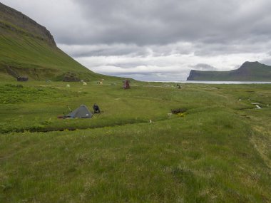 İzlanda, Batı fjords Hornstrandir, 29 Haziran 2018: Hornvik kamp manzaralı güzel Hornbjarg kayalıklardan yeşil çayır, su akışı ve tepeler, mavi deniz ve bulutlu gökyüzü arka plan ile uzak doğa rezerv.
