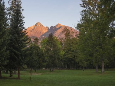 Tatra Dağları renkli pembe ve turuncu gündoğumu ışık menzil, yemyeşil ağaçlar ve otlar ile Tatranska Lomnice görüntüleyin. Erken sonbahar panorama.
