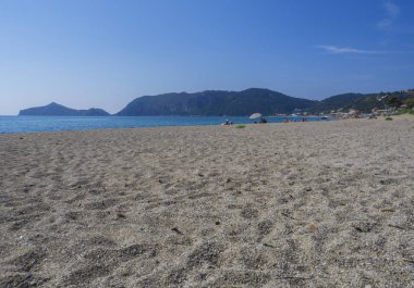Kum ve çakıl plaj ve Agios Georgios Pagon Corfu Island, Yunanistan ile güneşlenme halklar ve şemsiye manzaralı porto timony koyunda, turkuaz deniz sahilinde mavi gökyüzü artalan temizleyin.