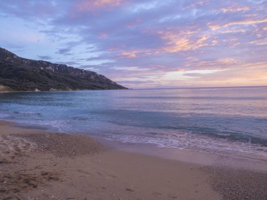 güzel pastel pembe turuncu ve altın günbatımı ve bulutlar dalgalar deniz sahilinde Agios Georgios Pagon beach Corfu Island, Yunanistan.