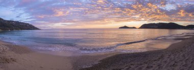 Panoramik güzel pastel pembe turuncu ve altın günbatımı bulutlar ve dalgalar deniz sahilinde Agios Georgios Pagon beach Corfu Island, Yunanistan.