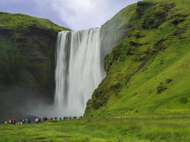 Güzel Skogafoss şelale içinde Güney İzlanda Skogar grup renkli giyinmiş turist insan ile uzun pozlama hareket bulanıklığı, kopya alanı