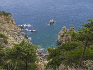 Paleokastritsa defne küçük kırmızı tekne ile cllifs, ağaçlar ve yeşil tepede görüntülemek, bulutlu gökyüzü, Corfu, Korfu, Yunanistan yaz