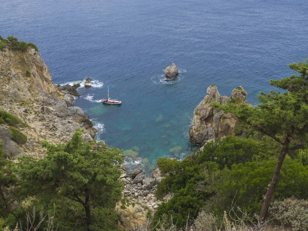 Kijk op cllifs, bomen en groene heuvel bij Paleokastritsa baai met kleine rode boot, zomer bewolkte hemel, Corfu, Crete, Griekenland — Stockfoto