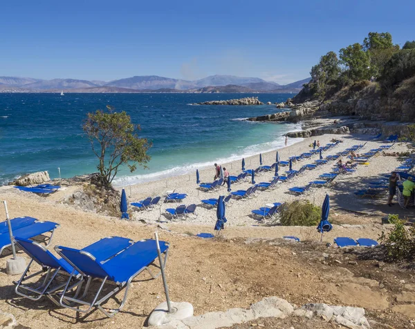 Kassiopi, Corfu Island, Yunanistan yolundaki mavi şezlong ve turist insanlar Kassiopi Bay ve Arnavut Dağları ile Bataria beyaz kum plaj görünümünü