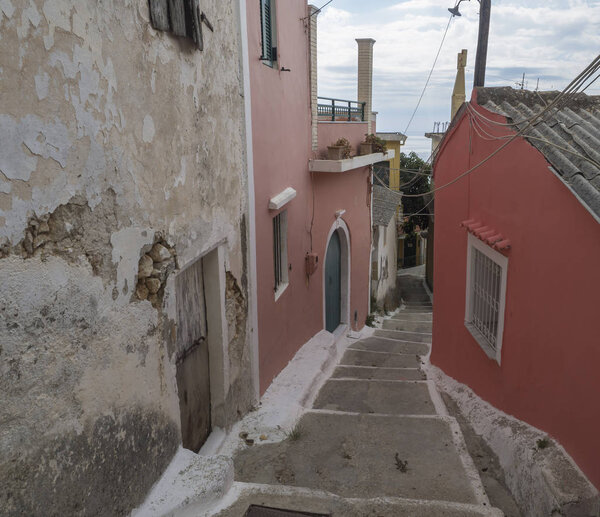 Narrow street and stairs with old red houses and green door, vintage look, Corfu Greece.