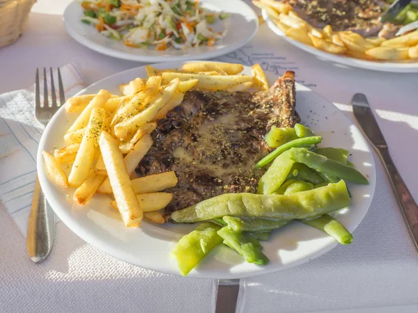 Geleneksel ev yapımı Yunan yemek, ızgara domuz biftek ile kızarmış patates ve yeşil çalı fasulyesi ve beyaz masa, doğal güneş ışığı salataya çiftçiler ile plaka kadar kapatın