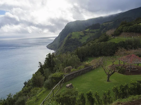 Breathtaking view with steep cliffs, sea, alcove and flower garden from the viewpoint Miradouro da Ponta do Sossego at Nordeste on Sao Miguel island, Azores, Portugal