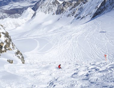 Free ride piste with snowboarder in red clothes skiing downhill on snow covered slopes from the top of Kitzsteinhorn mountain at Kaprun ski resort, National Park Hohe Tauern, Austrian Alps, Europe