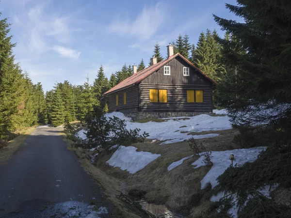 Chalet à colombages, cabane en rondins à côté de la route asphaltée dans la montagne Jizerske Hory au printemps avec forêt luxuriante d'épinettes verdoyantes et neige au soleil, fond de ciel bleu — Photo