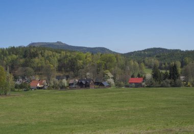 Geleneksel ahşap yazlık ve yemyeşil çim çayır, huş yaprak döken ve ladin ağaç orman ve tepeler, mavi gökyüzü arka plan ile Lusitian dağlarında köy Marenice görünümü ile Bahar manzara