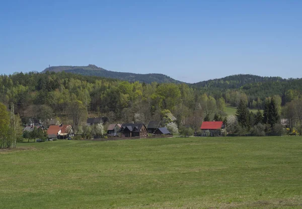 Paisaje primaveral con vista al pueblo de Marenice en las montañas de Lusitian con casa de campo de madera tradicional y exuberante prado de hierba verde, abedul caducifolio y abeto bosque y colinas, fondo azul cielo — Foto de Stock