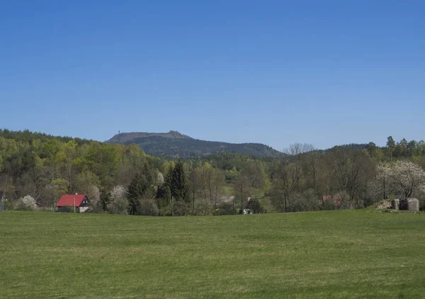 Paesaggio primaverile con vista sul villaggio di Marenice nelle montagne lusiziane con cottage in legno tradizionale e prato di erba verde lussureggiante, betulla latifoglie e abete rosso foresta e colline, sfondo cielo blu — Foto Stock