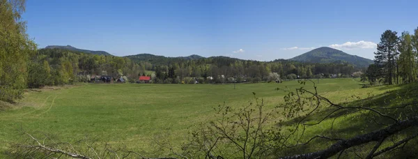 Panoramic landscape with view on village Marenice in Lusitian mountains with traditional wooden cottage and lush green grass meadow, deciduous and spruce tree forest and hills, spring, blue sky