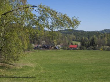Geleneksel ahşap yazlık ve yemyeşil çim çayır, huş yaprak döken ve ladin ağaç orman ve tepeler, mavi gökyüzü arka plan ile Lusitian dağlarında köy Marenice görünümü ile Bahar manzara