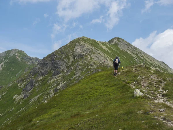 Hermoso paisaje de montaña de las montañas occidentales de Tatra o Rohace con los hombres excursionista con mochila sendero de senderismo en la cresta. Picos rocosos verdes agudos de la montaña. Verano cielo azul nubes blancas . — Foto de Stock