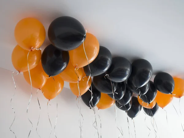 Manojo de globos de aire naranja y negro para Halloween o cumpleaños sobre fondo de techo blanco. Vacaciones, decoración y concepto de fiesta — Foto de Stock
