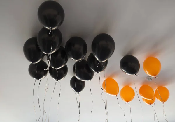 Manojo de globos de aire naranja y negro para Halloween o cumpleaños sobre fondo de techo blanco. Vacaciones, decoración y concepto de fiesta — Foto de Stock