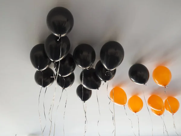 Manojo de globos de aire naranja y negro para Halloween o cumpleaños sobre fondo de techo blanco. Vacaciones, decoración y concepto de fiesta — Foto de Stock