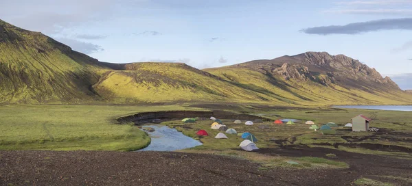 Panoramic landscape with colorful tents at camping site on blue Alftavatn lake with green hills and glacier in beautiful landscape of the Fjallabak Nature Reserve in the Highlands of Iceland part of