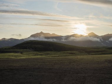 Alftavatn kamp alanında güneş doğuyor. Arkasında karla kaplı dağlar, yeşil tepeler ve buzul var. İzlanda 'nın dağlık bölgelerindeki Fjallabak Doğa Koruma Alanı' nın yaz manzarası. Boşluğu kopyala.