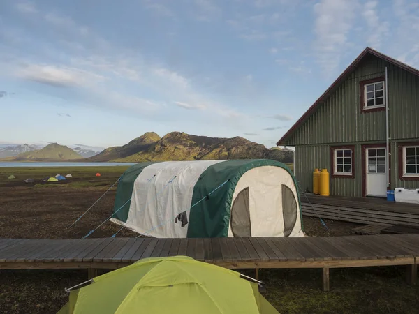 Coloridas tiendas de campaña y cabaña turística verde en el camping Alftavatn con lago azul y verdes colinas y glaciares en el fondo. Paisaje de la Reserva Natural de Fjallabak en las tierras altas de Islandia — Foto de Stock