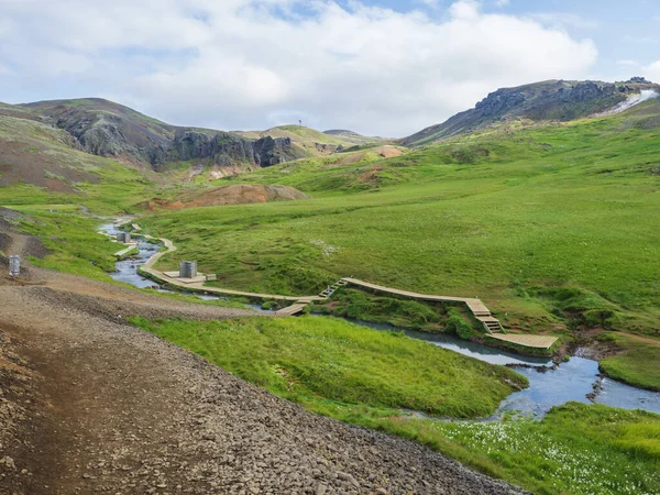 Baño geotermal natural en un arroyo Hot River en el valle de Reykjadalur con sendero de madera y vestuarios. Islandia del Sur cerca de la ciudad de Hveragerdi. Mañana soleada de verano — Foto de Stock