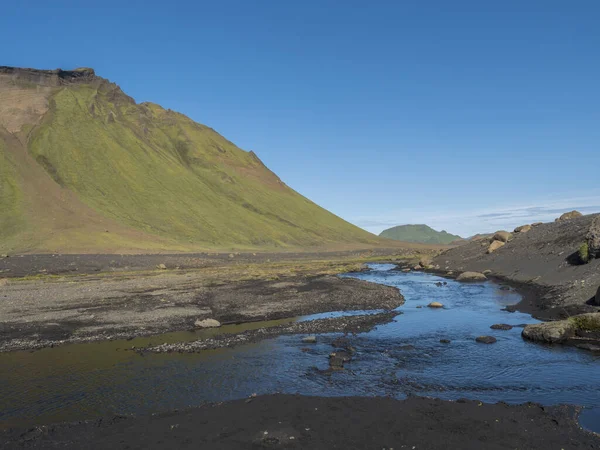 Modrý říční potok a zelená Hattafell hora v sopečné krajině za Emstrur kempu v oblasti Fjallabak přírodní rezervace v regionu Vysočina na Islandu — Stock fotografie