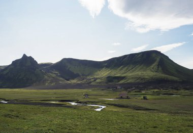 view on Hvanngil mountain hut and camp site with green hills, river stream and lush grass and moss. Laugavegur hiking trail, Fjallabak Nature Reserve, Iceland. Summer blue sky