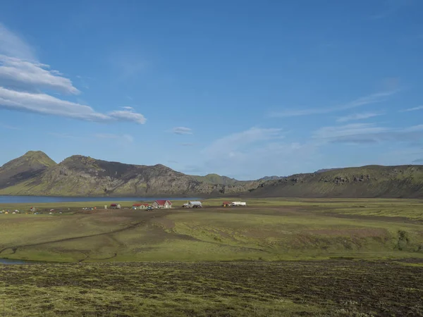 Paisaje con cabañas de montaña en el camping en el lago azul Alftavatn con río, colinas verdes y glaciar en el hermoso paisaje de la Reserva Natural de Fjallabak en las Tierras Altas de Islandia parte de —  Fotos de Stock