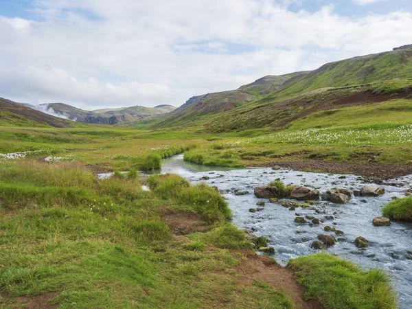 Valle de Reykjadalur con aguas termales río con exuberante prado de hierba verde y colinas con vapor geotérmico. Islandia del Sur cerca de la ciudad de Hveragerdi. Mañana soleada de verano, cielo azul . — Foto de Stock