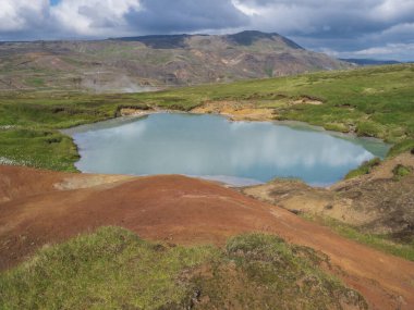 Reykjadalur Vadisi 'nde sıcak kaynak nehri ve yemyeşil çayır ve jeotermal buharlı tepeleri olan havuz. Güney İzlanda, Hveragerdi şehri yakınlarında. Yaz güneşli sabah, mavi gökyüzü.