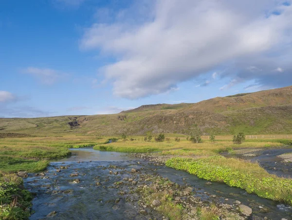 Río azul, exuberante prado de hierba verde y colinas en el área de aguas termales de Reykjadalur, al sur de Islandia, cerca de la ciudad de Hveragerdi. Mañana soleada de verano, cielo azul . — Foto de Stock