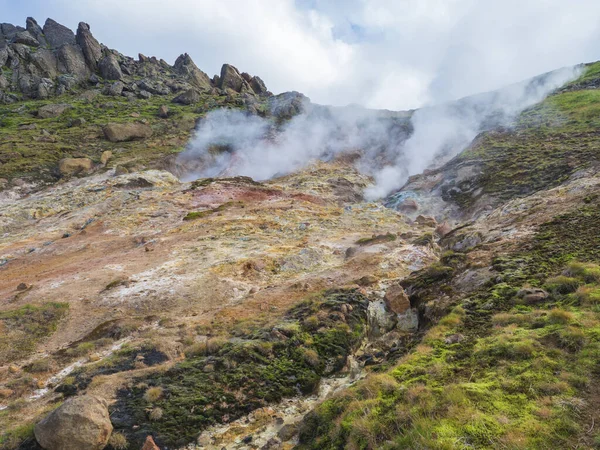 Színes rhyolit piros, narancs és sárga fumarole a Reykjadalur völgyben éles sziklákkal, fűvel és geotermikus gőzzel. Dél-Izland Hveragerdi város közelében. Nyári napsütéses nap — Stock Fotó