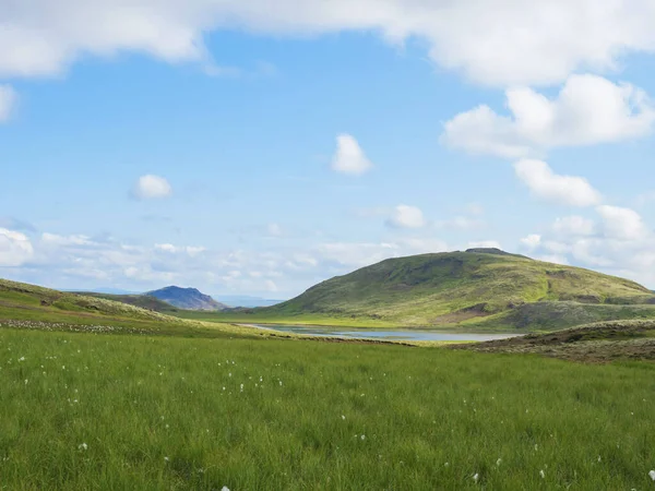 Błękitne jezioro, bujna zielona trawa łąka i wzgórza w obszarze gorących źródeł Reykjadalur, Południowa Islandia w pobliżu miasta Hveragerdi. Letni słoneczny poranek, błękitne niebo. — Zdjęcie stockowe