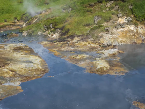 Forró geotermikus kék sár medence Reykjadalur völgyében buja zöld fű rét és gőz. Dél-Izland közelében Hveragerdi város. — Stock Fotó