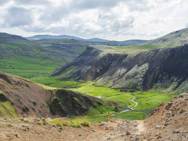Reykjadalur valley with hot springs river, lush green grass meadow, rocks and hills with geothermal steam. South Iceland near Hveragerdi city. Summer sunny morning, blue sky.