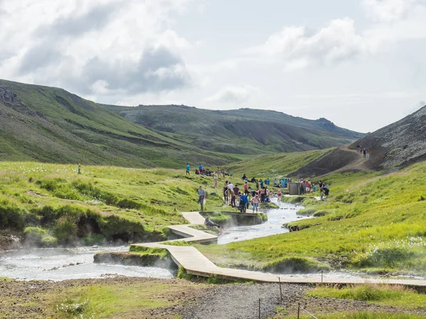 İzlanda, Hveragerdi, 5 Ağustos 2019: Reykjadalur Vadisi 'ndeki bir sıcak nehir deresinde kalabalık bir doğal jeotermal banyo, bir grup banyo, insanları ve turistleri rahatlatan, ahşap patika ve değişen bir yol.