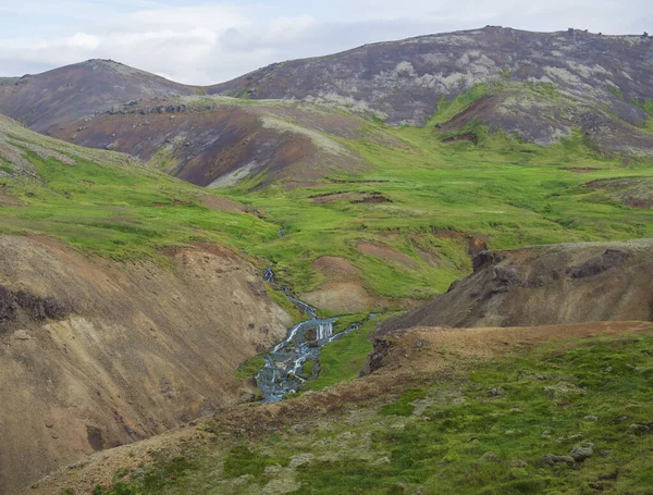 Reykjadalur völgy forró forrásokkal folyó, buja zöld fű rét, sziklák és hegyek geotermikus gőz. Dél-Izland Hveragerdi város közelében. Nyári napsütéses reggel, kék ég. — Stock Fotó