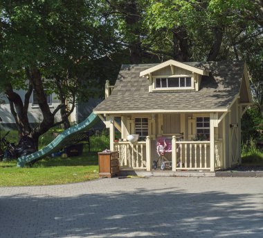 Iceland, Hveragerdi, August 5, 2019: Big cute wooden children house on garden with slide for the childrens games, pink pram and furniture