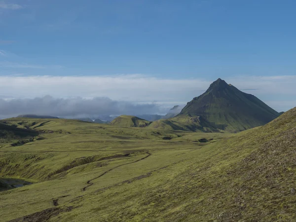 Sopečná krajina s pěšinou Laugavegur trek a zelená Storasula hora s bujným mechem a nízkými mraky. Přírodní rezervace Fjallabak, Island. Modrá obloha pozadí, kopírovat prostor. — Stock fotografie