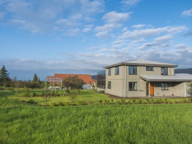 İzlanda, Hveragerdi, 5 Ağustos 2019: Huzurlu İzlanda manzaralı, yemyeşil çayır ve yaz mavi gökyüzü, beyaz bulutlu aile evleri inşa etmek.