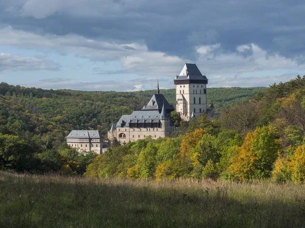 Karlstejn castelo de estado gótico perto de Praga, o castelo mais famoso da República Checa com grama prado e outono árvores coloridas e floresta. Céu azul nuvens fundo. Localizado perto de Praga . — Fotografia de Stock