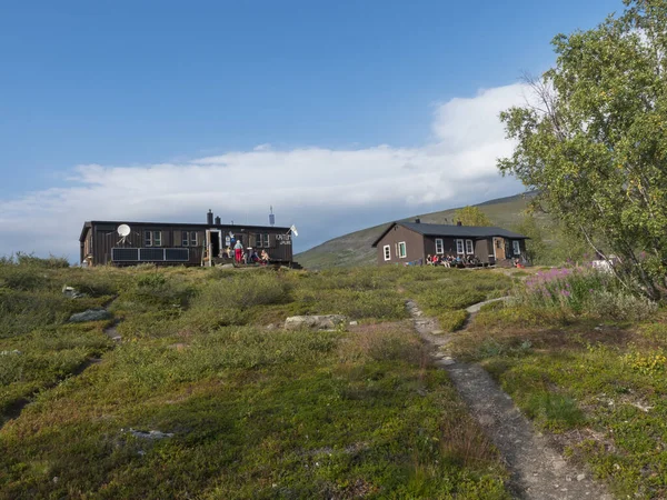 Kaitumjaure, Norrbotten, Suecia, 27 de agosto de 2019: STF Kaitumjaure Cabaña de montaña con excursionistas e invitados en reposo en grupo. Colinas verdes, bosque de abedules y sendero de senderismo Kungsleden. Verano azul — Foto de Stock